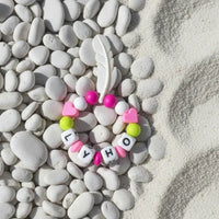 Anneau de dentition Lyho en silicone assorti aux couleurs anis et fushia avec plume blanche de 6 cm.